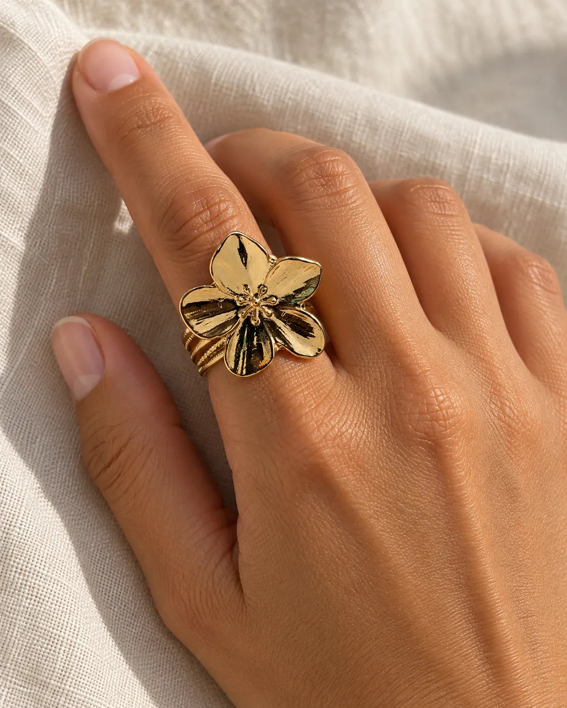 Hand resting on linen wearing the gold flower statement ring