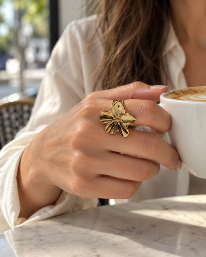 Hand holding a coffee cup wearing the gold bloom ring