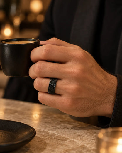 Hand holding an espresso cup in a dim cafe wearing the black ring