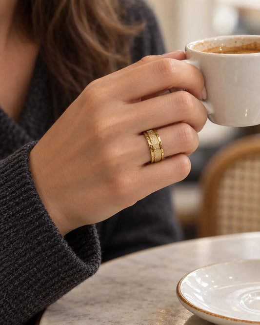 Hand wearing the gold textured band ring while holding a coffee cup