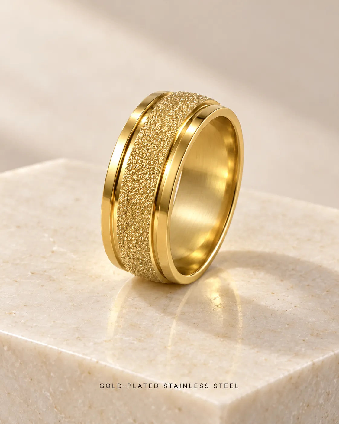 Gold textured band ring standing on a pale marble block