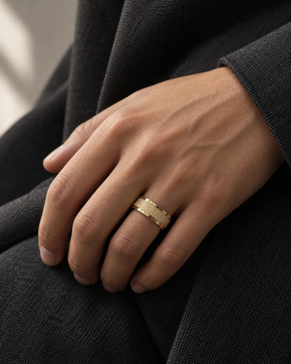 Hand wearing the gold band ring against dark clothing