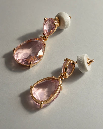 Pair of pink crystal teardrop earrings with push-backs on a grey surface