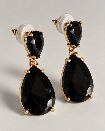Pair of black crystal teardrop earrings with push-backs on a grey surface