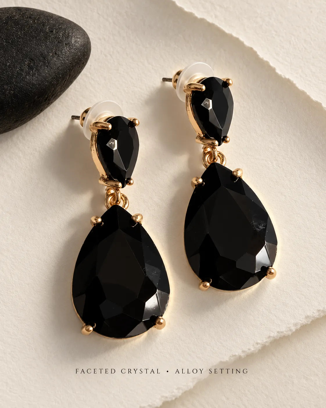 Black crystal teardrop earrings displayed on a cream stone surface