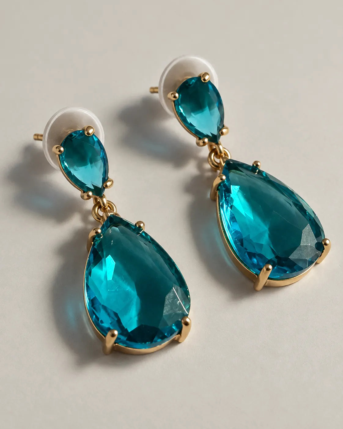Pair of teal-blue crystal teardrop earrings with push-backs on a grey surface