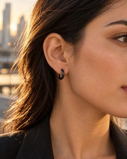 Profile close-up of a black stainless steel huggie hoop on the ear