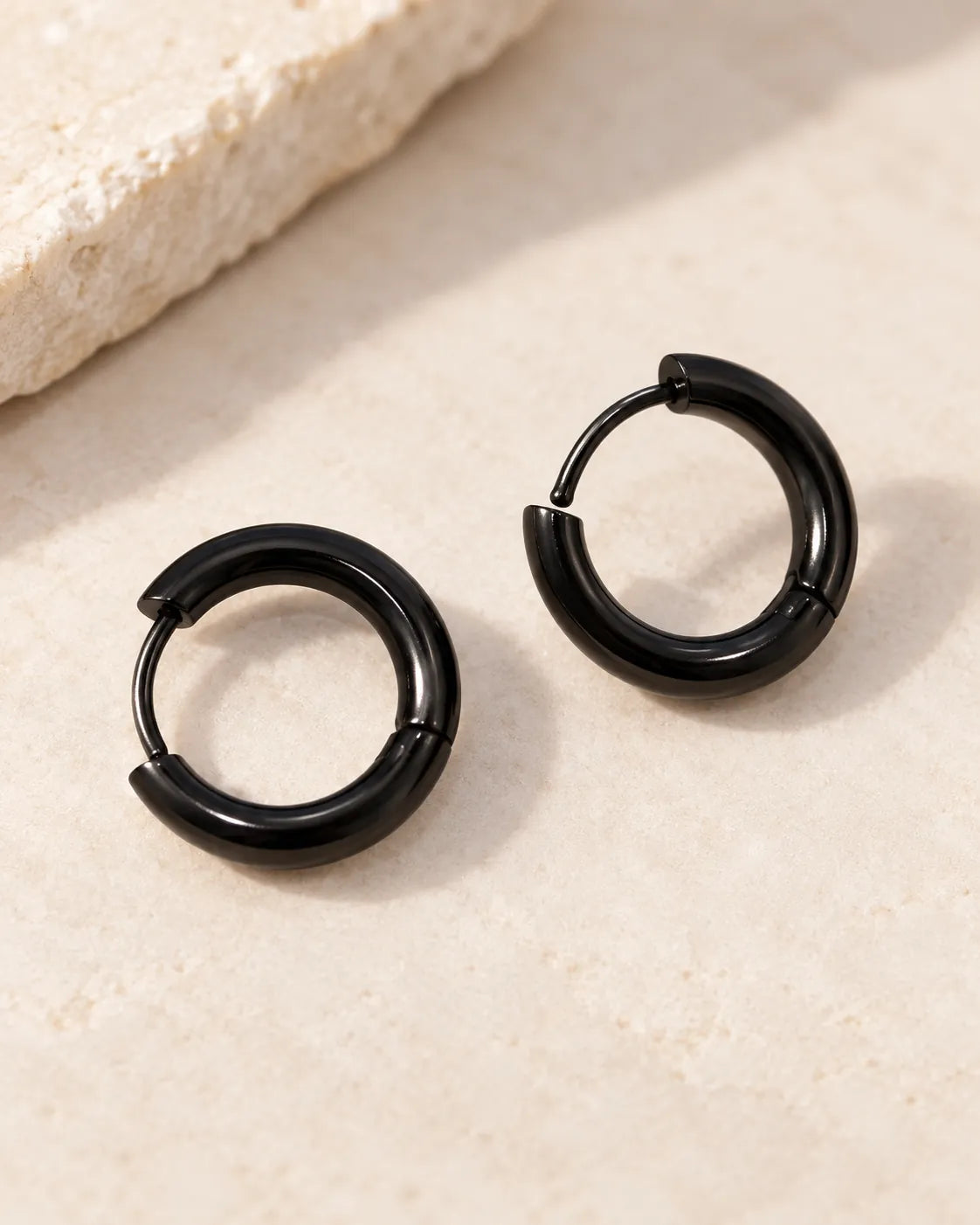 Pair of black stainless steel huggie hoop earrings on a stone surface
