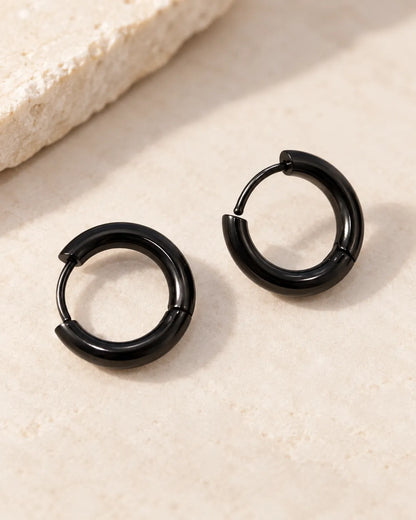 Pair of black stainless steel huggie hoop earrings on a stone surface