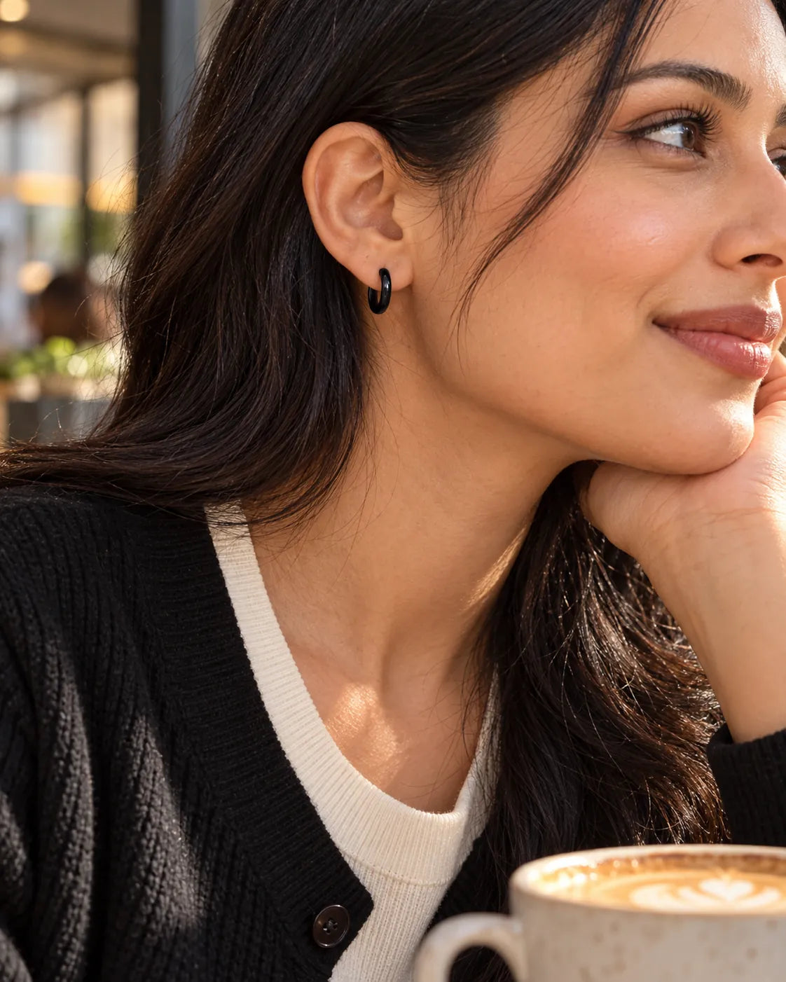 Model at a café wearing small black huggie hoop earrings
