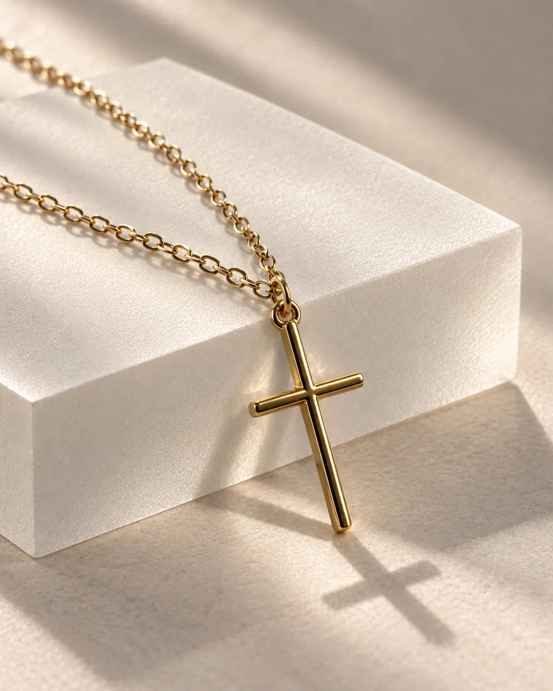 Gold-tone cross pendant draped over a white block with a soft shadow