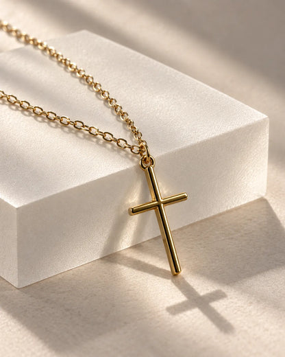 Gold-tone cross pendant draped over a white block with a soft shadow