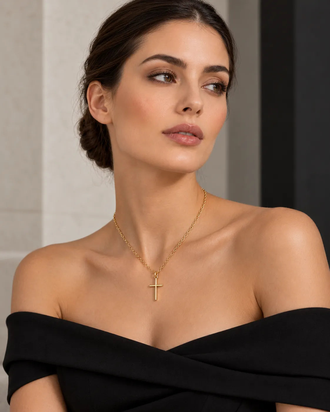 Model in an off-the-shoulder black top wearing the gold cross necklace
