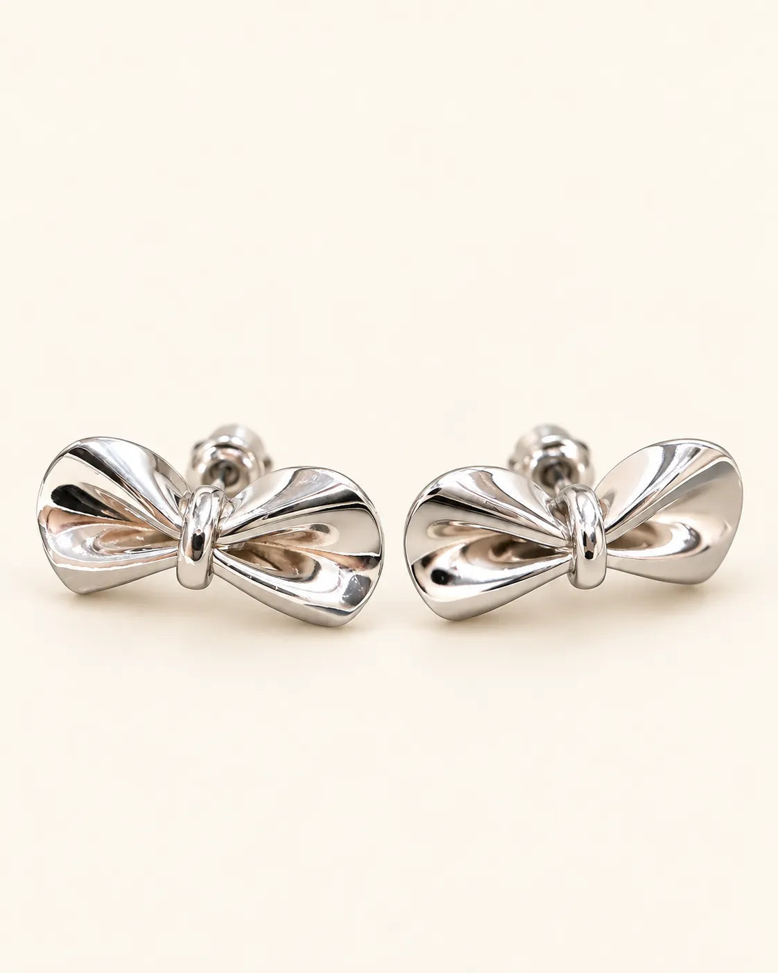 Pair of polished silver-tone bow stud earrings on cream