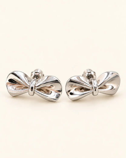 Pair of polished silver-tone bow stud earrings on cream