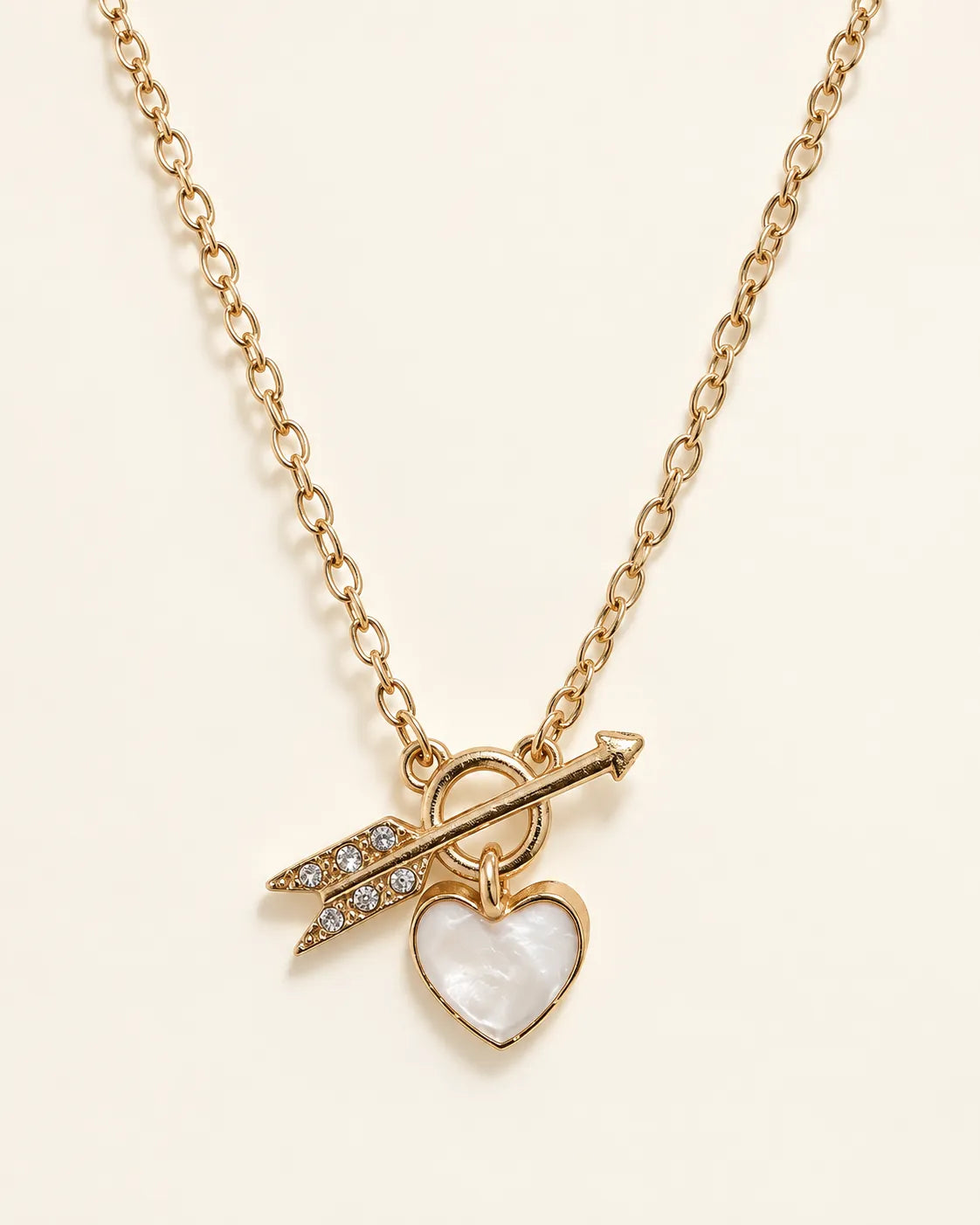 Gold-tone Amélie heart and arrow toggle necklace on a cream background