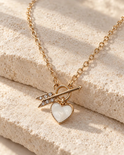 Gold heart and arrow toggle necklace draped over a stone block