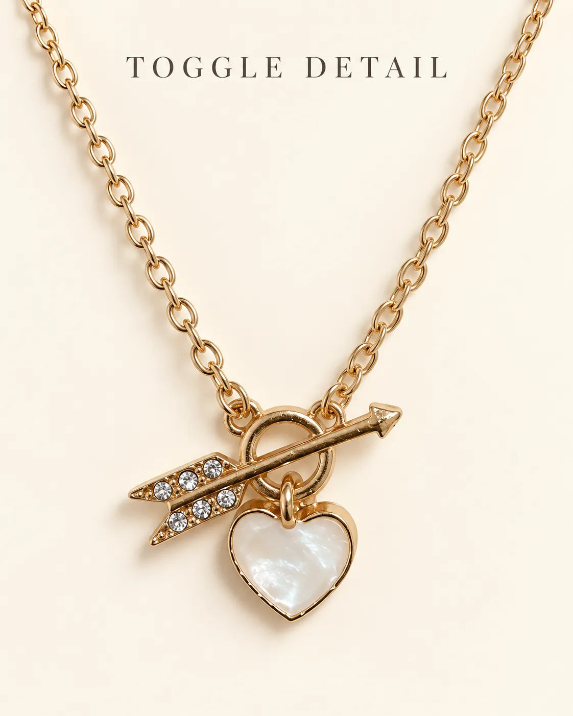 Gold toggle necklace with Toggle Detail text on a cream background