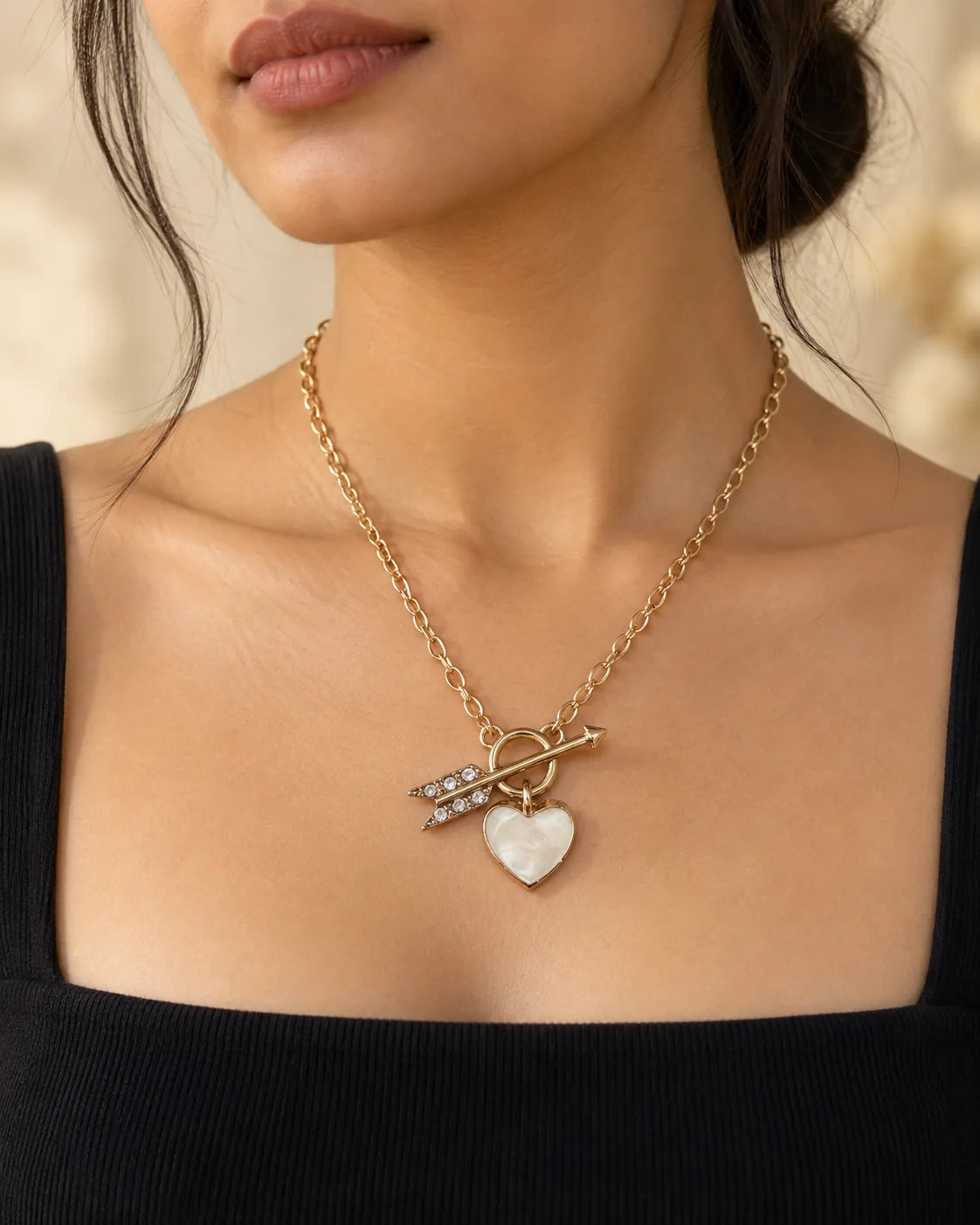 Model in a black square-neck top wearing the gold heart and arrow pendant