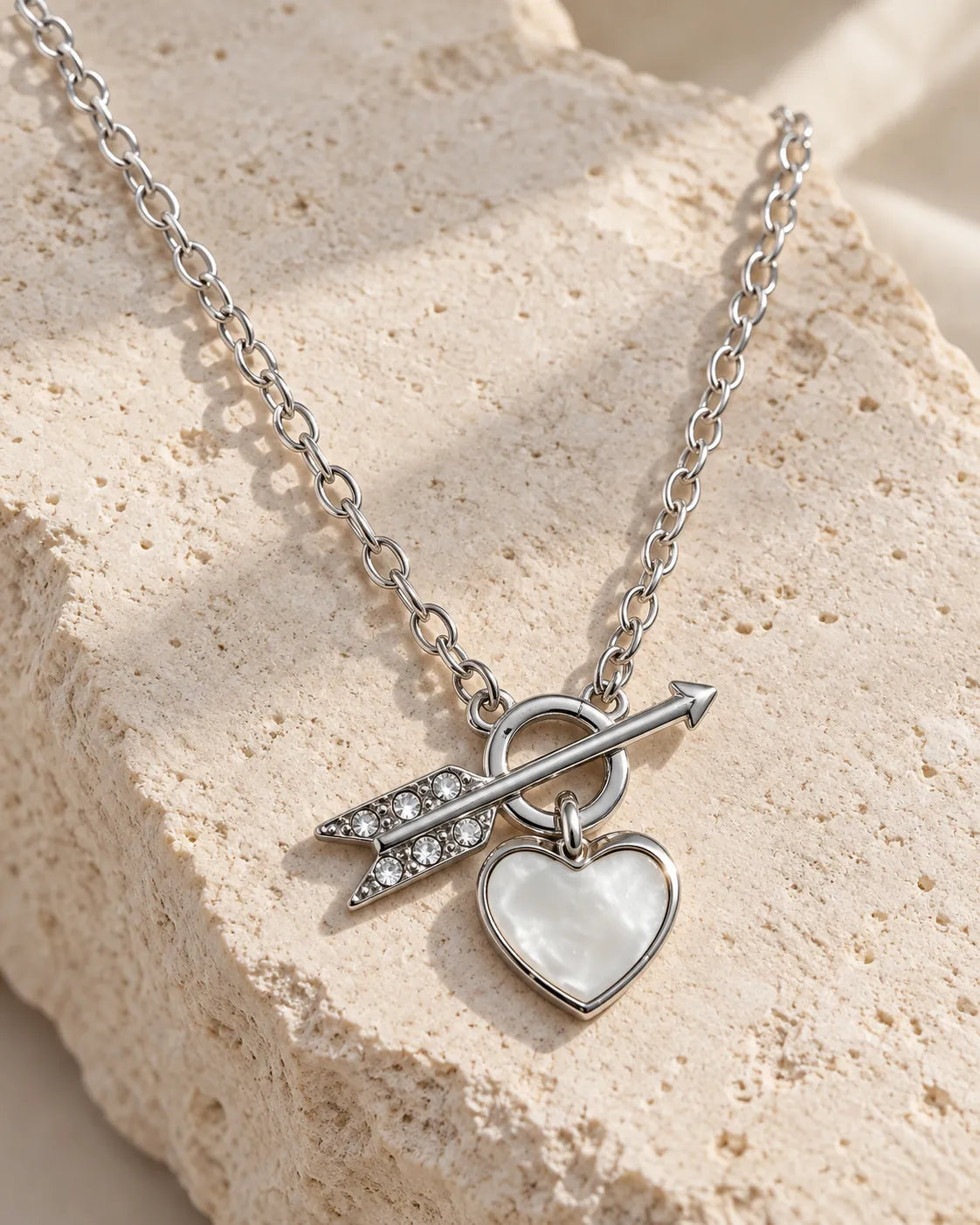 Silver toggle heart necklace draped over a textured stone block