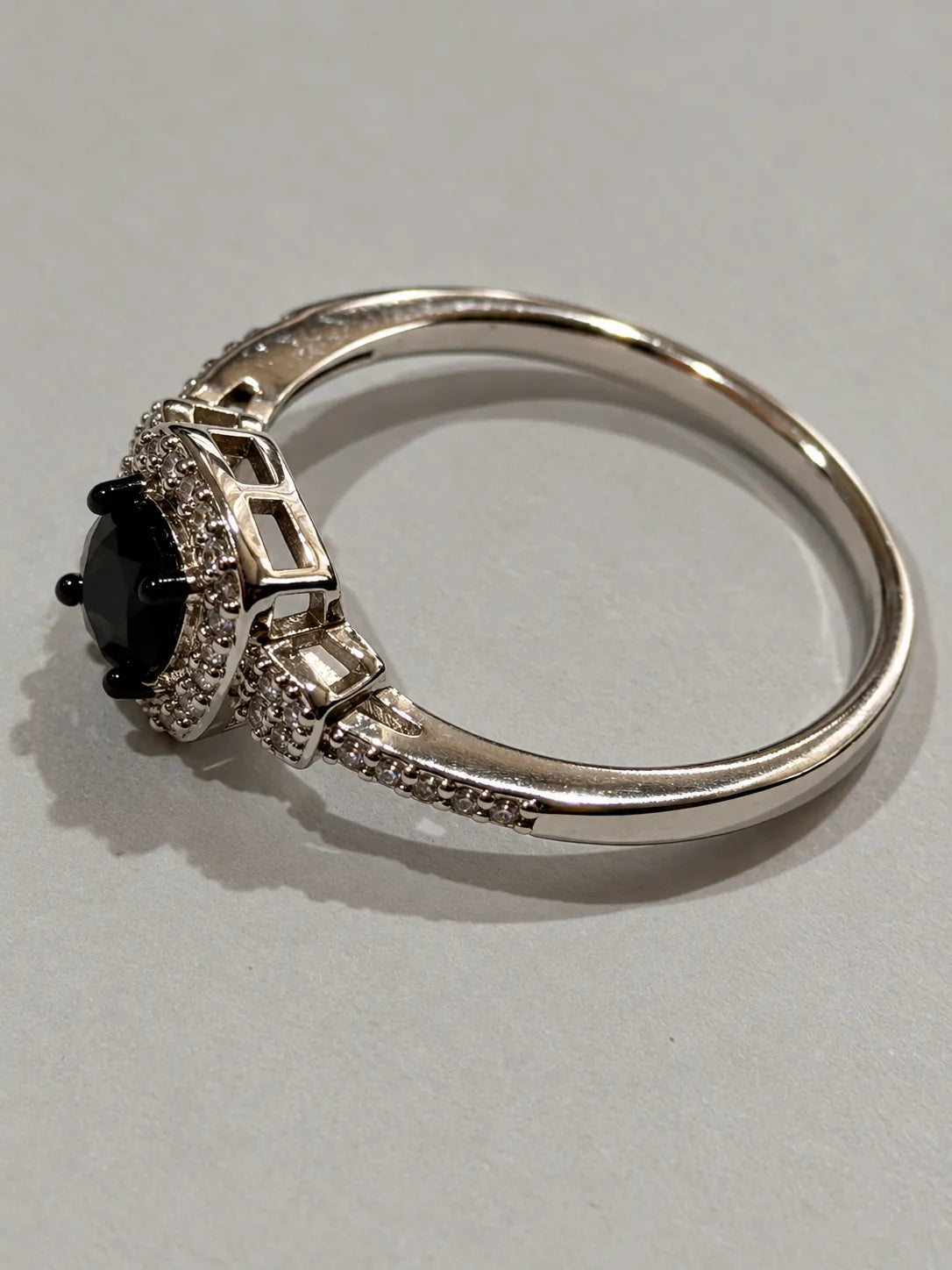 Angled view of the black and white cubic zirconia halo ring on grey