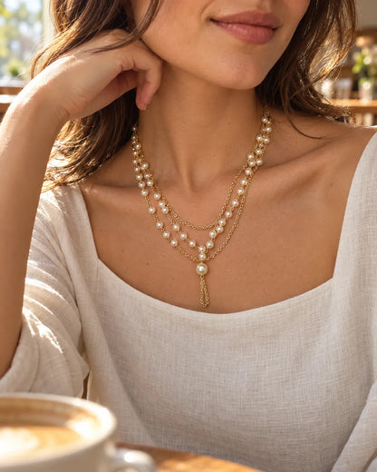 Model at a café in a cream knit wearing the layered pearl-style necklace