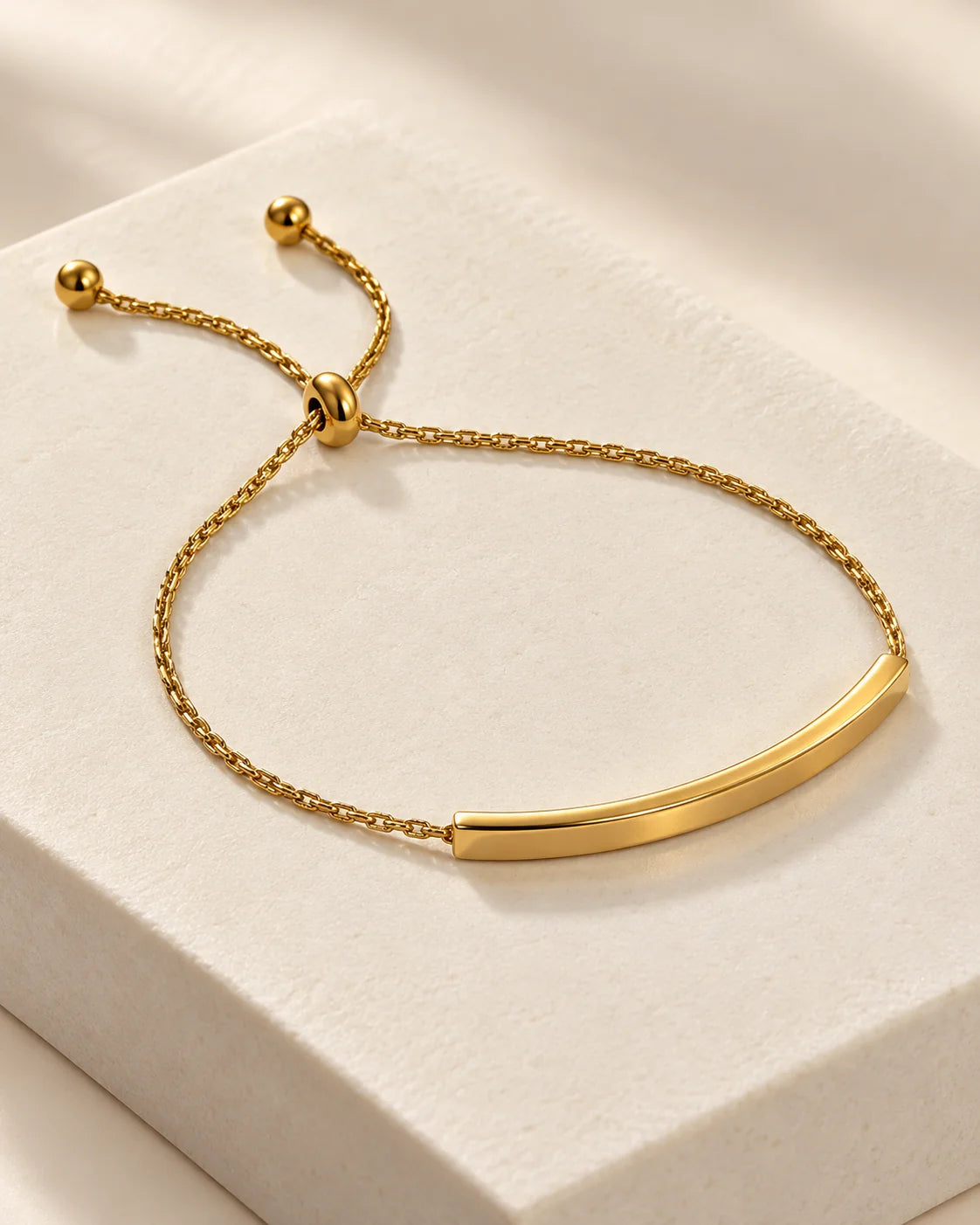 Aria 18K gold plated curved bar slider bracelet on a white stone plinth