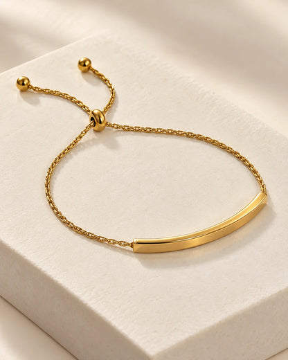 Aria 18K gold plated curved bar slider bracelet on a white stone plinth