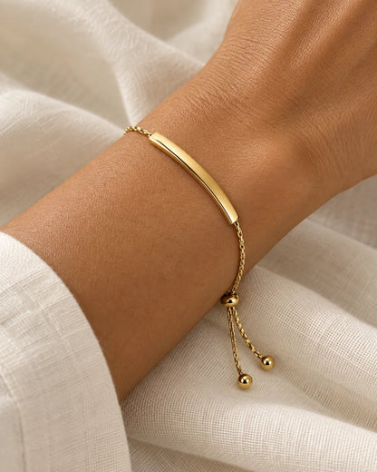 Gold-tone sliding bar bracelet worn on the wrist against ivory linen