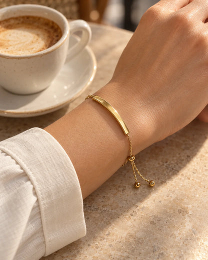 Gold bar bracelet worn on the wrist beside a morning espresso