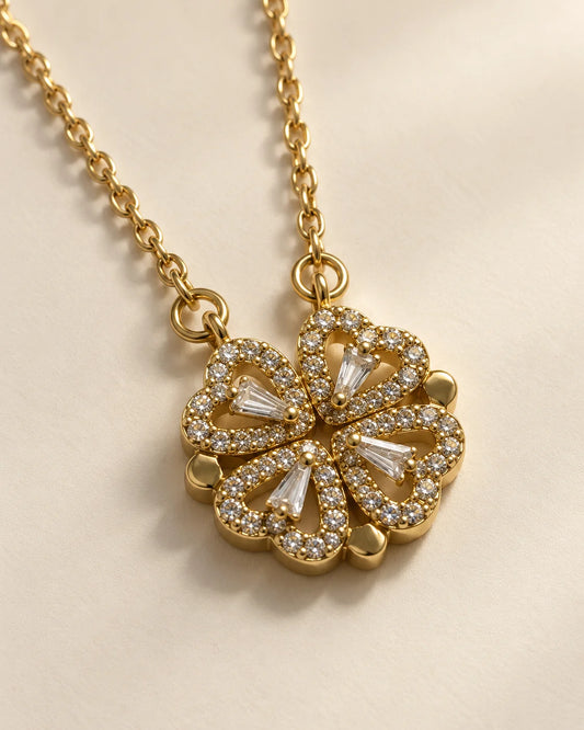 Amora gold four-heart clover pendant with sparkling cubic zirconia on a cream background