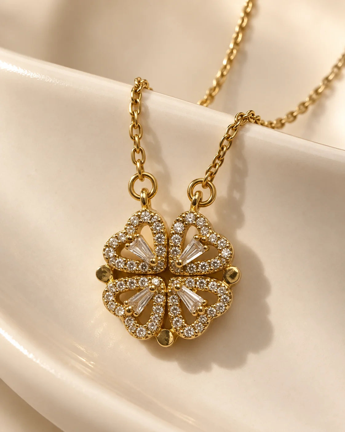 Amora gold four-heart clover necklace draped over an ivory ceramic dish
