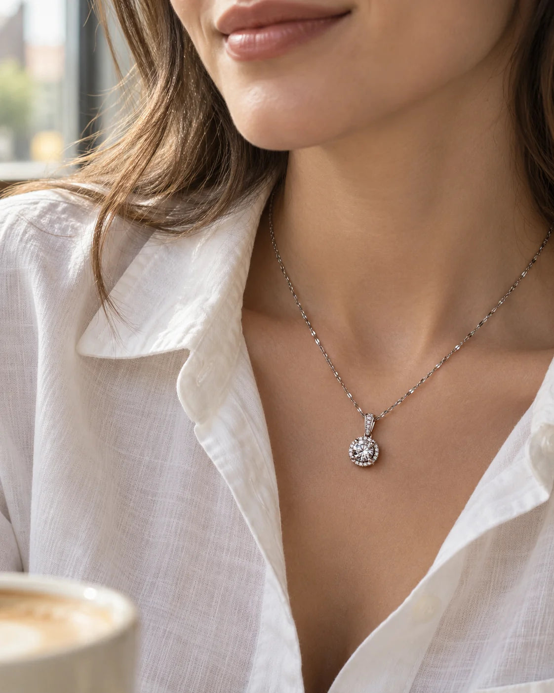 Model in a white shirt wearing the Luna silver halo necklace by a café window