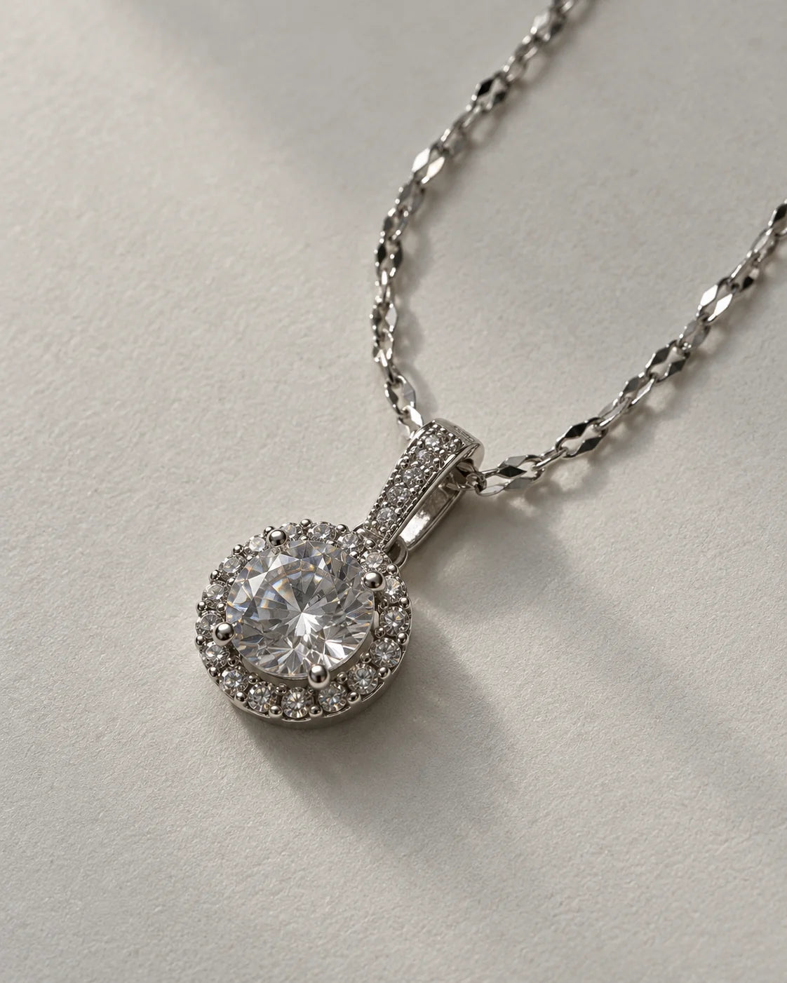 Luna silver round halo pendant on a faceted link chain against soft grey