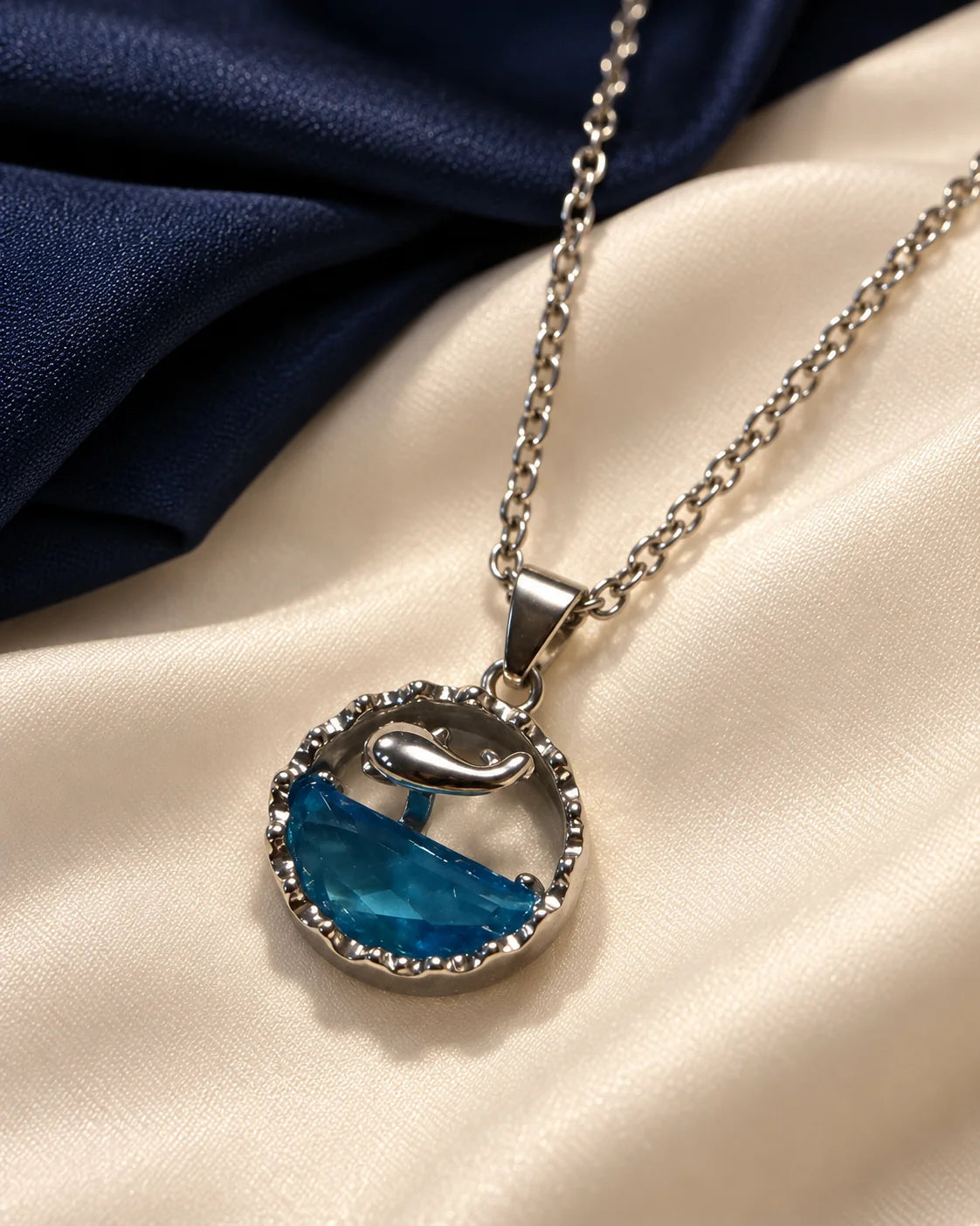 Delphine ocean blue dolphin pendant on cream satin with a navy backdrop