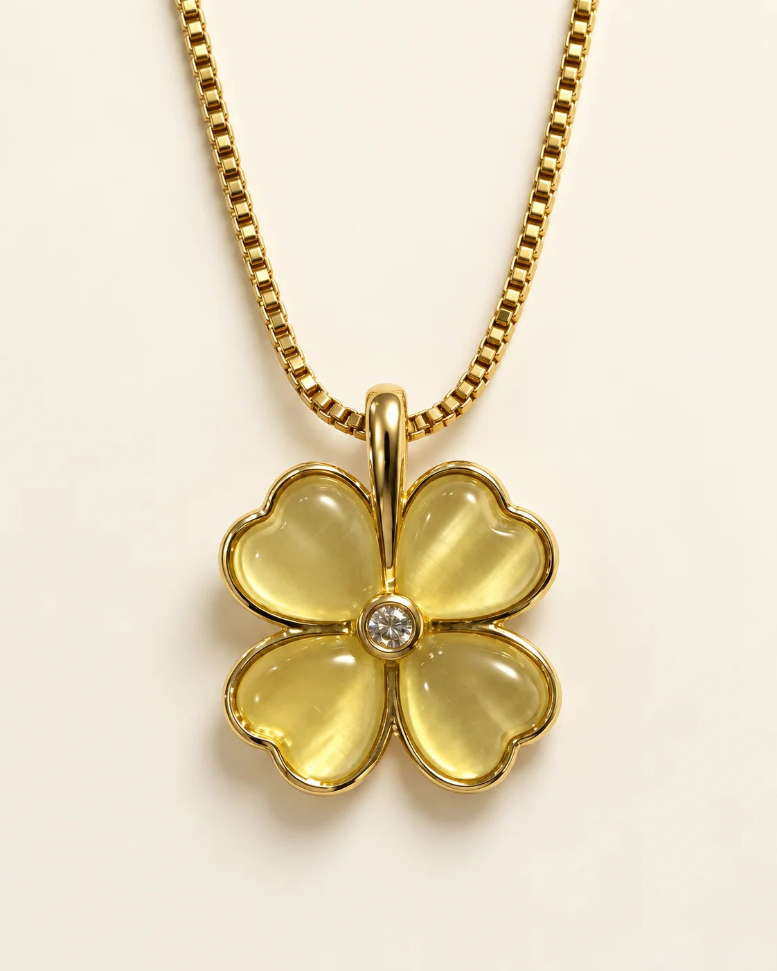 Primrose gold four-petal heart clover pendant with soft yellow petals on a cream background