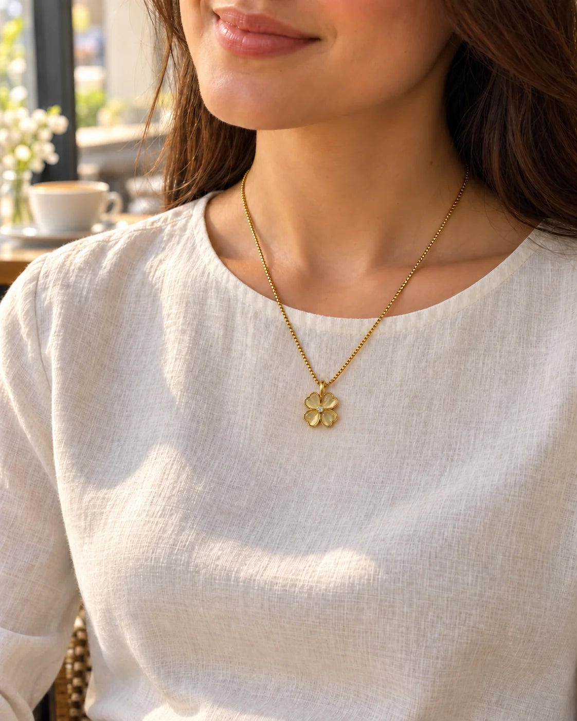 Model in a white top wearing the Primrose clover necklace in a café