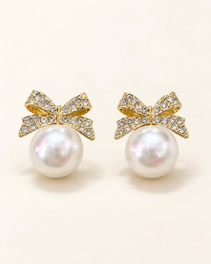Pair of gold rhinestone bow stud earrings with large pearl-look beads on cream
