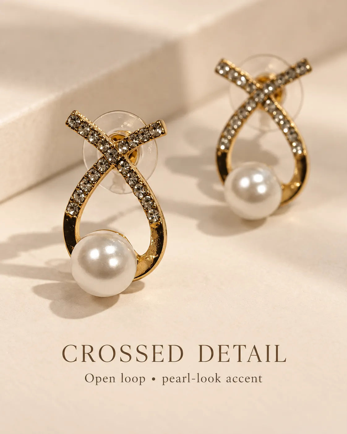Gold crossed loop pearl-look studs on cream with Crossed Detail text