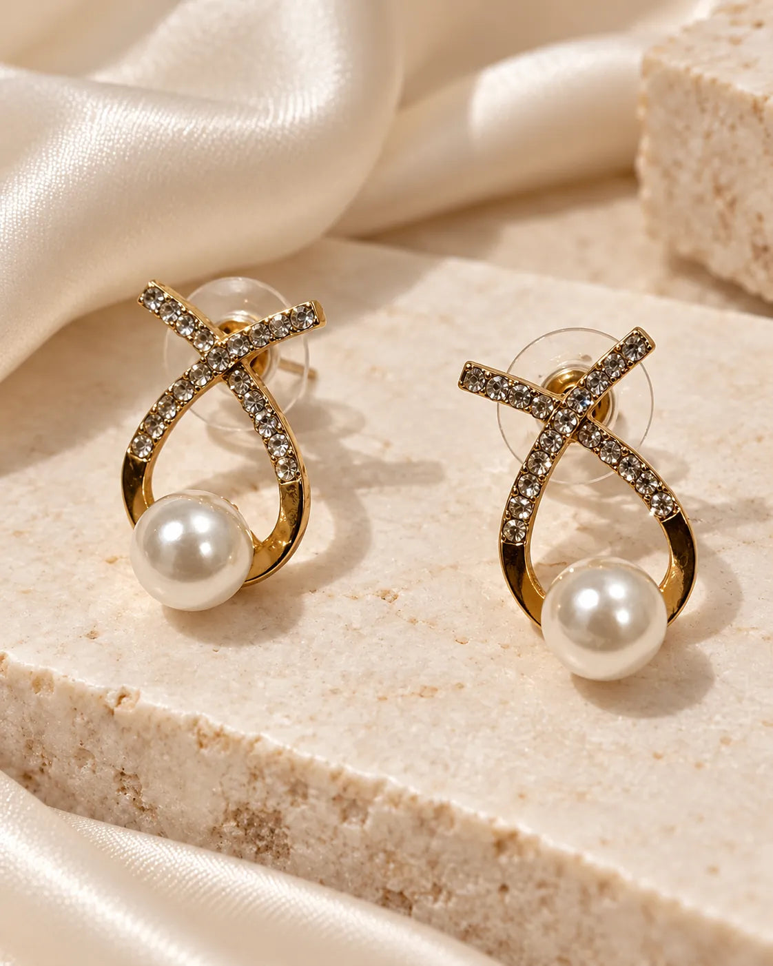 Gold rhinestone crossed loop studs on stone beside draped satin