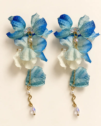 Blue and white fabric flower statement drop earrings on a cream background