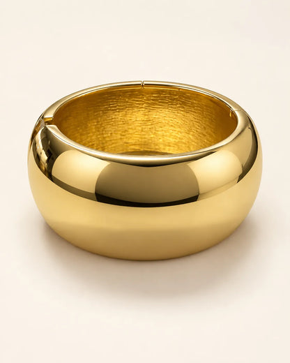 Wide polished gold statement cuff bracelet on a cream background