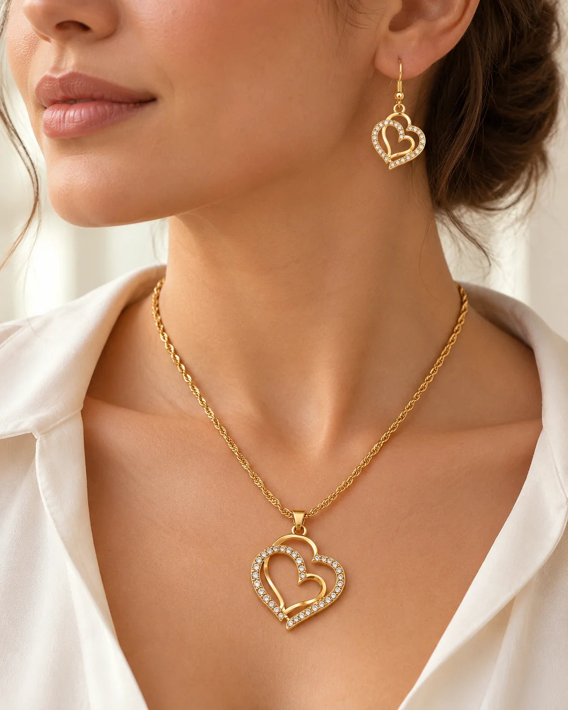 Woman wearing the gold double heart necklace and earrings with a white shirt