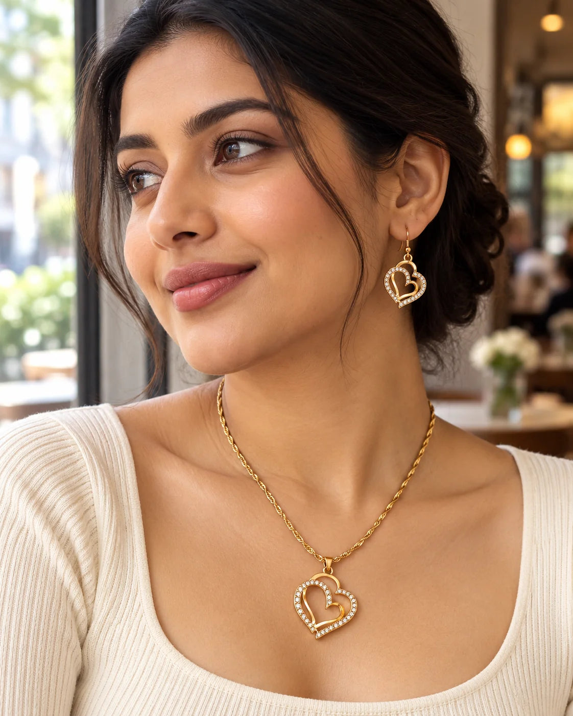 Woman in a café wearing the Everlinked gold double heart necklace and earrings