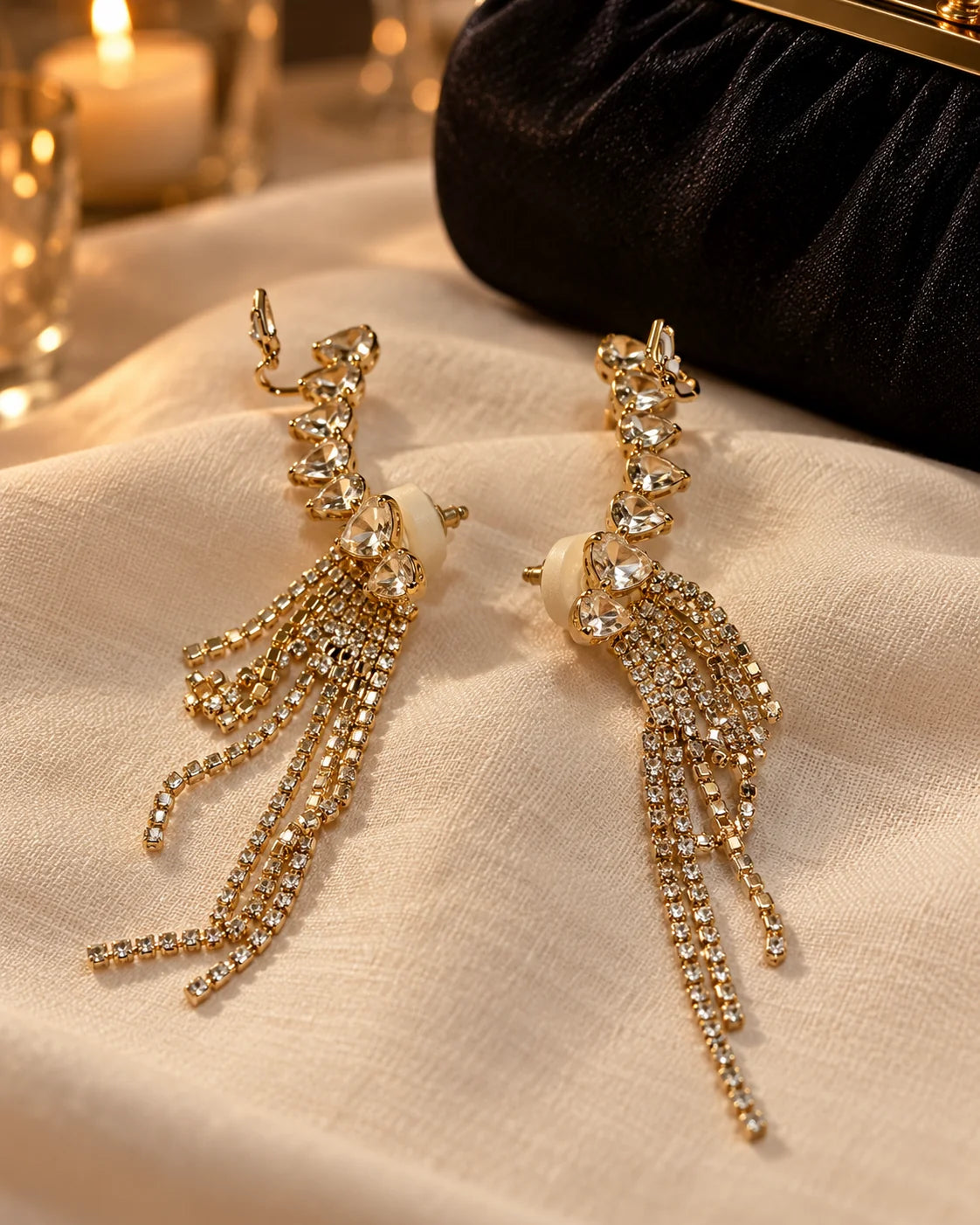 Gold heart ear climber earrings on ivory linen beside a black evening clutch