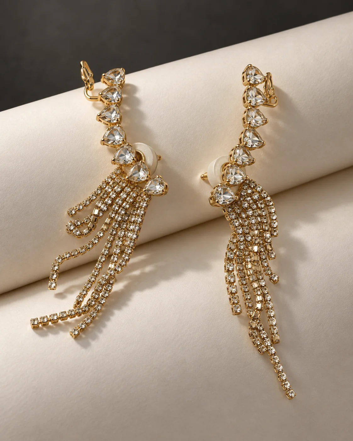 Pair of gold heart crystal tassel ear climbers draped over ivory satin