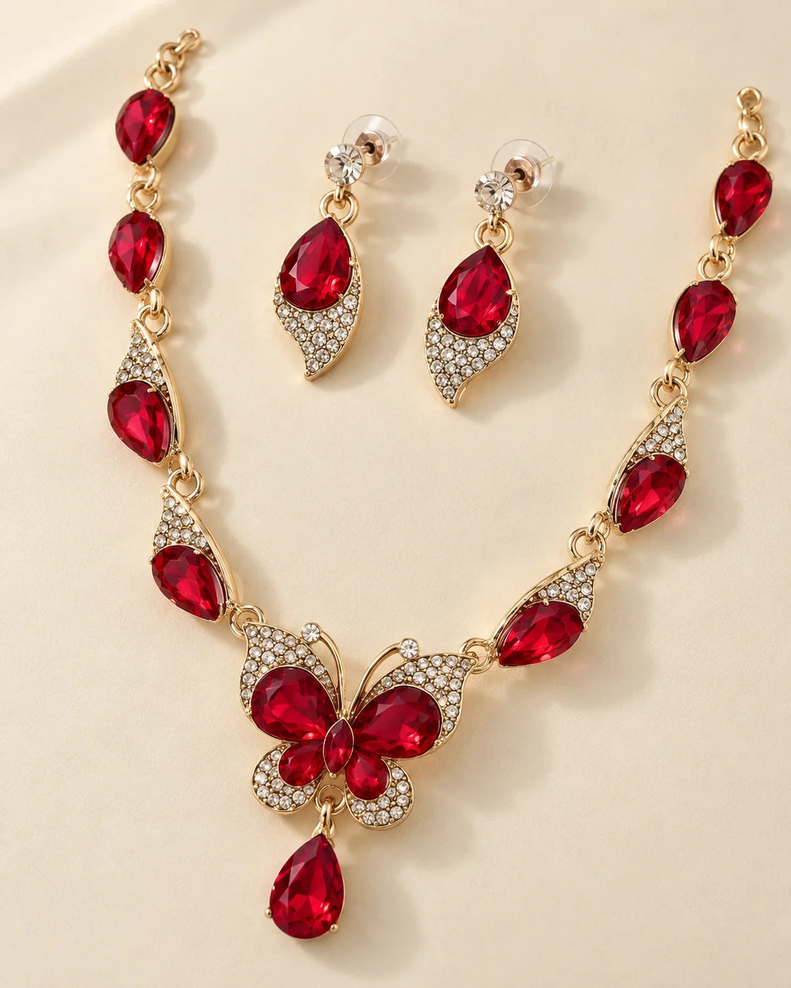 Red butterfly necklace with matching red teardrop drop earrings on a cream background