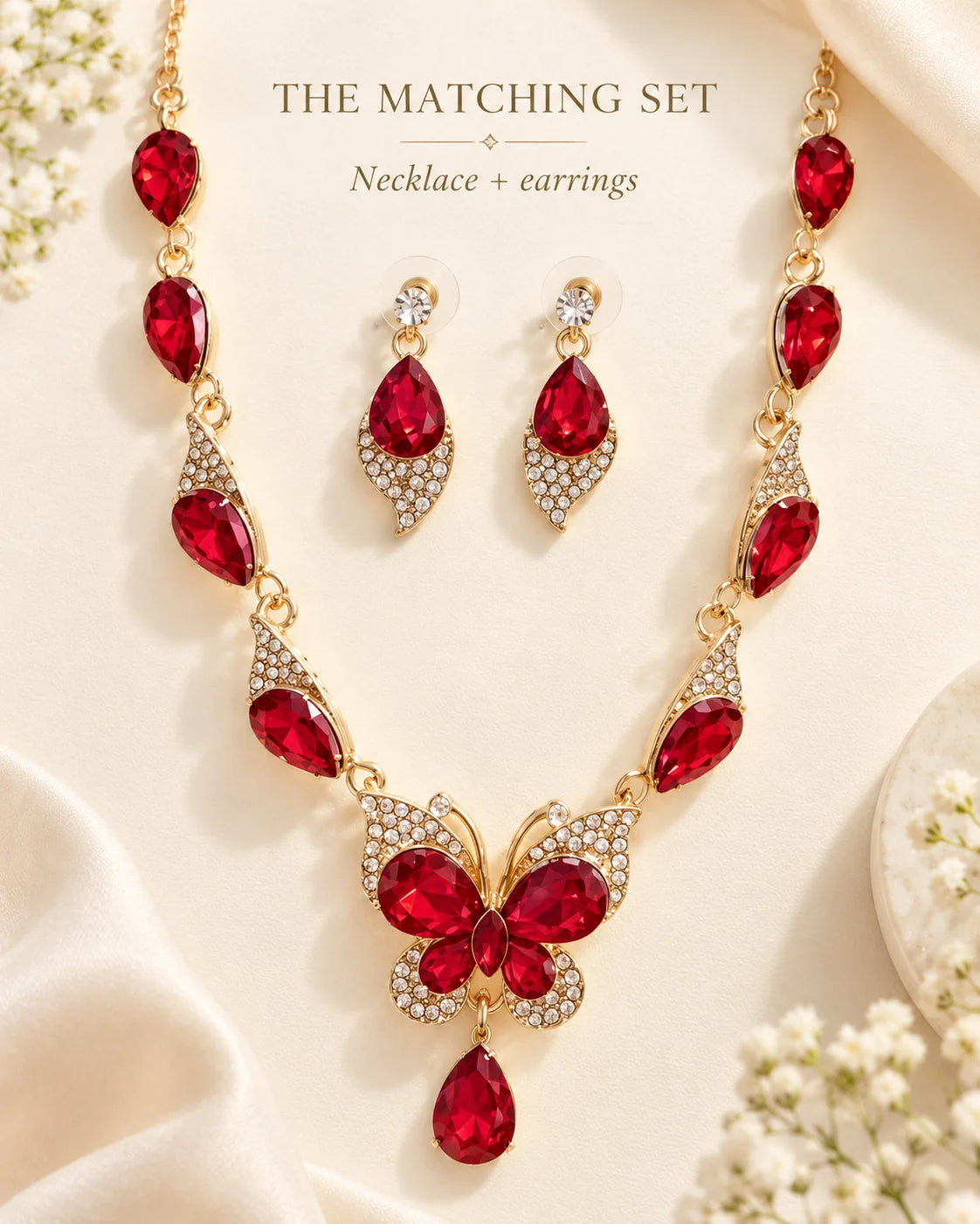 The matching set: red butterfly necklace and earrings styled on cream with flowers