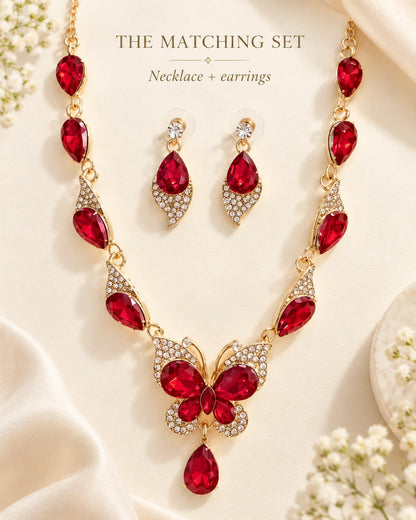 The matching set: red butterfly necklace and earrings styled on cream with flowers