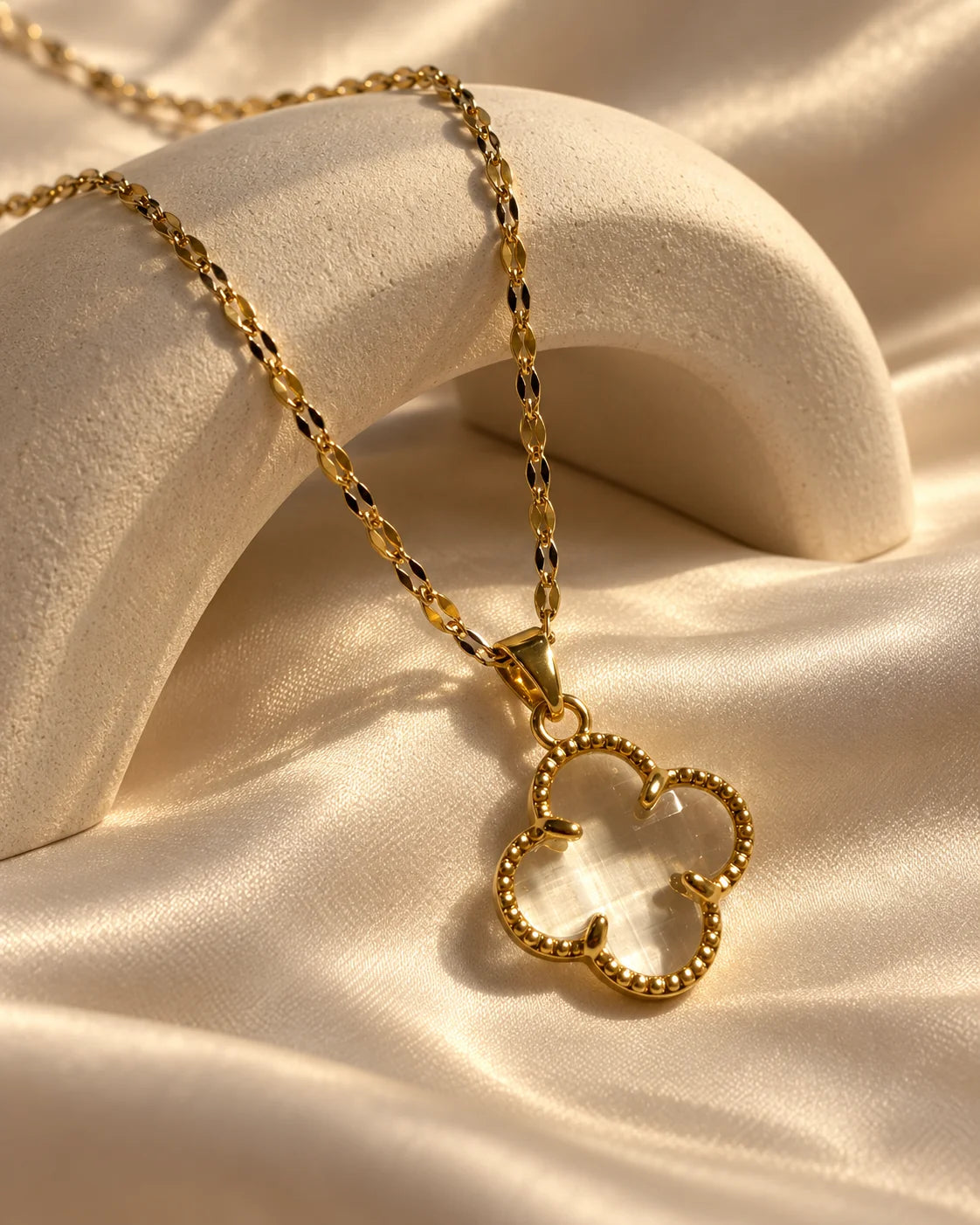 Fortuna clear clover necklace draped over an ivory arch on cream satin
